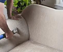 Professional upholstery cleaner deep-cleaning a fabric sofa with a handheld extraction tool and hose in Indianapolis, IN.